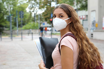 COVID-19 Beautiful student girl with protective mask walking in city street. College girl back to school after pandemic coronavirus disease 2019.