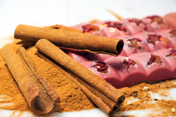 Bar of pink chocolate with raisins and fruits on a background of cinnamon sticks close up