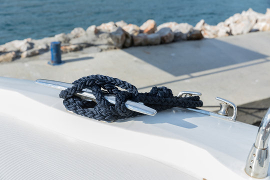 Detail of an anchor rope on a yacht, Stainless steel boat mooring cleat with knotted rope mounted on white yacht deck