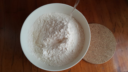 Flour,tremors, salt, sugar, water in a white bowl on a wooden table. Cooking process. Pancakes recipe. 