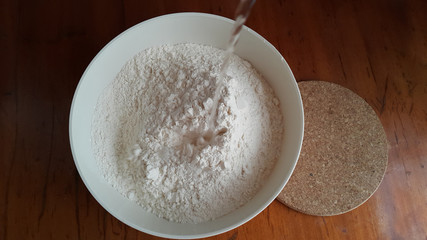 Flour,tremors, salt, sugar, water in a white bowl on a wooden table. Cooking process. Pancakes recipe.	
