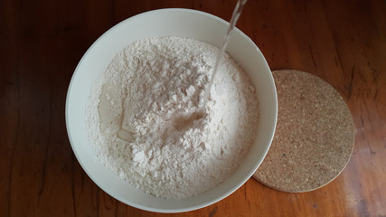 Flour,tremors, salt, sugar, water in a white bowl on a wooden table. Cooking process. Pancakes recipe. 