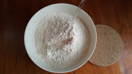 Flour,tremors, salt, sugar, water in a white bowl on a wooden table. Cooking process. Pancakes recipe.	
