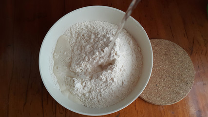 Flour,tremors, salt, sugar, water in a white bowl on a wooden table. Cooking process. Pancakes recipe.	
