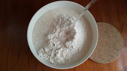 Flour,tremors, salt, sugar, water in a white bowl on a wooden table. Cooking process. Pancakes recipe.	
