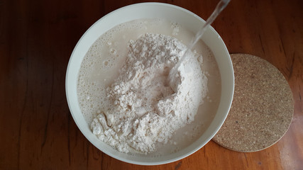 Fototapeta na wymiar Flour,tremors, salt, sugar, water in a white bowl on a wooden table. Cooking process. Pancakes recipe. 
