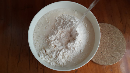 Flour,tremors, salt, sugar, water in a white bowl on a wooden table. Cooking process. Pancakes recipe. 