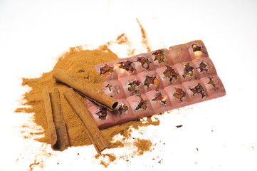 Bar of pink chocolate with raisins and fruits on a background of cinnamon sticks close up