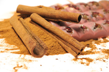 Bar of pink chocolate with raisins and fruits on a background of cinnamon sticks close up