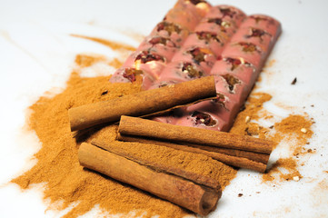 Bar of pink chocolate with raisins and fruits on a background of cinnamon sticks close up