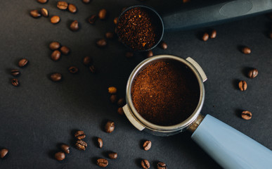 Coffee filter holder with ground coffee beans and coffee beans on a black background