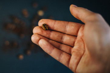 Coffee bean in male hand on black background