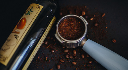 Coffee holder, ground coffee beans and coffee syrup on black background