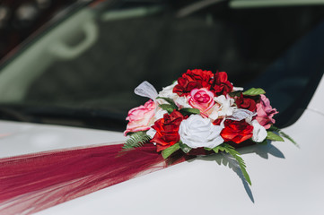The wedding bouquet and artificial flower decorations are attached with a ribbon on the hood of the car.