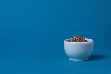 a bowl of cumin isolated on blue background. Image contains copy space