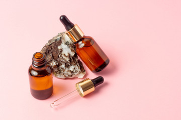 An amber bottle for essential oils and cosmetics stands next to the stone. Glass bottle on a pink...