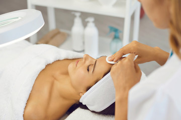 Cosmetologist cleaning woman facial skin with cotton pads before beauty treatment