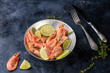 Fresh large shrimp with lime, sprigs of razmarin, ice on a dark background, close-up.