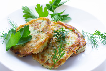 zucchini pancakes on a white plate with parsley leaves.