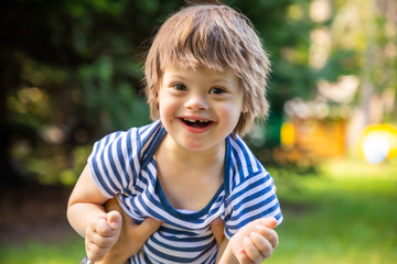 Portrait of baby boy with Down syndrome playing in summer day on nature