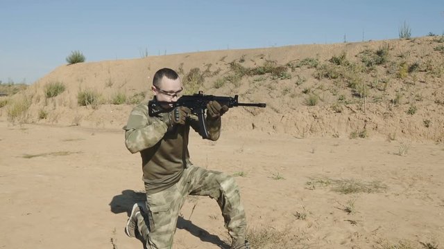 Portrait of a young man in camouflage clothes aiming and shooting outdoors alone. Slow motion video.
