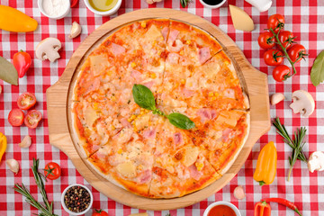 Hawaiian Italian pizza with parmesan cheese, pineapple, corn, ham toppings, fresh basil and tomatoes sauce on a wooden board, rustic village background, top view. European cuisine