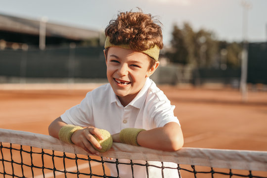 Cheerful boy with tennis ball on court