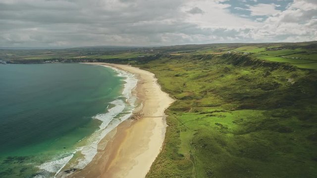 Hyperlapse Irish coast aerial view: sand beach with water waves. Wonderful Atlantic ocean seascape in summer daytime. Green countryside of Northern Ireland. Cinematic zooming footage shot in 4K, UHD