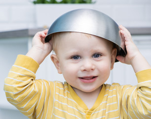 boy smiling with a bowl on his head. games in the kitchen.