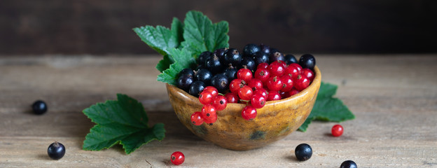 Red and black currant berries in ceramic bowl on a wooden background, banner
