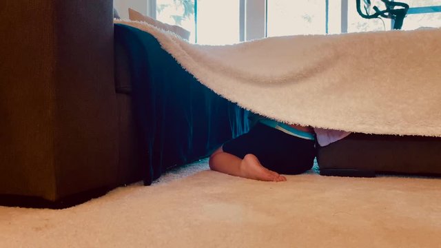 little boy hiding under a made up fort 