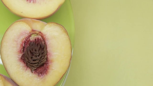 close-up half of peach fruit with stone rotates on a green-yellow background. Copy space