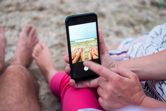 The family takes pictures of their feet with a phone camera. The concept of a beach family vacation on the seaside.