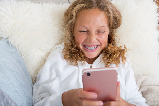 Tween, Preteen, Mixed Race Girl with braces laughs while using her smart phone