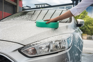 Female hands hold with green sponge and foam washing her car