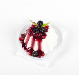 Dessert cream pudding with sauce and fresh berries on a plate on a white background top view