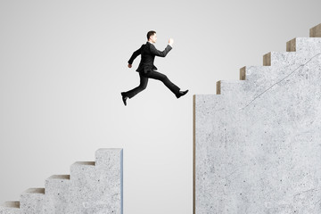 Young businessman jumping on stairs on gray background.