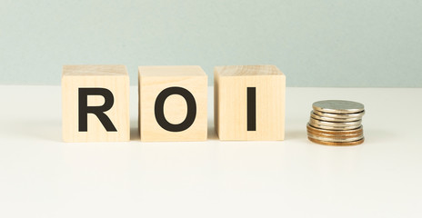 Three wooden cubes with letters ROI stands for Return on Investment on white board.