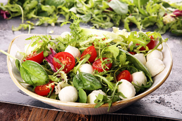 Mix fresh leaves of arugula, lettuce, spinach, beets for salad on table. Salad with tomato
