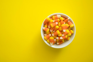 Colorful Candy Corn in a Bowl on a Yellow Background with Room for Copy