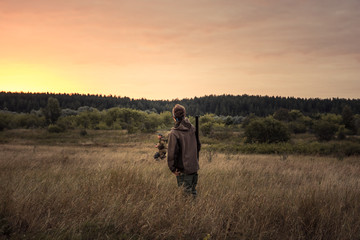 Fototapeta na wymiar Hunter men during hunting standing in rural field and looking into the distance at beautiful sunset 