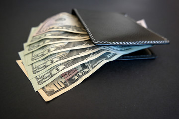 american banknotes in black leather wallet on dark surface