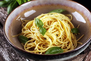 Plate of delicious spaghetti pesto garnished with parmesan cheese and basil on rustic dark background