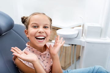 Very happy emotional child sitting on a dental chair and showing perfect healthy white smiling. Kid teeth treatment