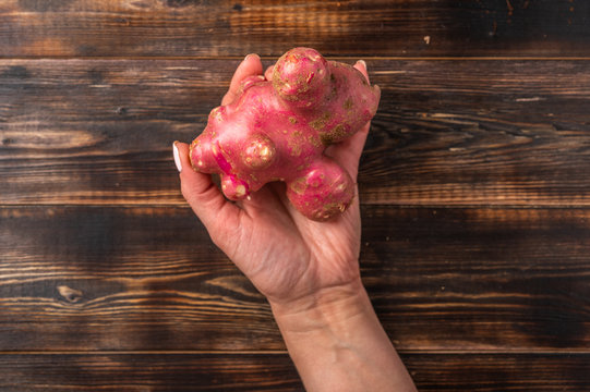 Womans hand holds trendy ugly organic potato from home garden on on a wooden background, unnormal vegetable or food waste concept, copy space