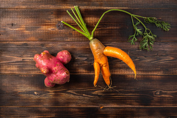 Trendy ugly organic carrot with the halm and potato from home garden on on a wooden background,...