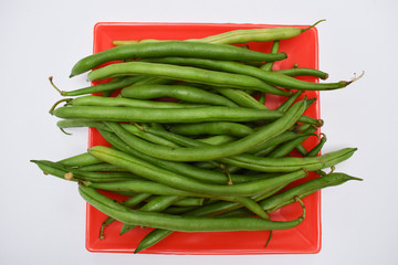 Fresh french beans Indian vegetables oon red plate with white background. Green beans bunch many veg fresh organic raw