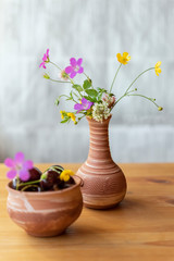 Bouquet of bright colorful wildflowers and ripe cherries in a clay vases on a wooden table, summer farm rustic concept. Selective focus