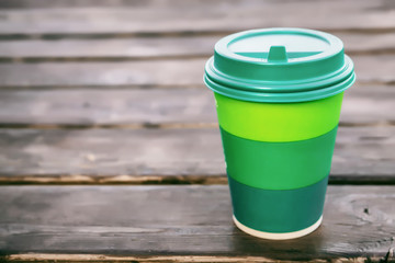 green cardboard cup with plastic lid for coffee on wooden background