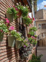 Flower pots with colorful flowers hanging from a brick wall in a Spanish village